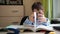 the boy shows a trick with a book. a teenager with glasses is doing homework. textbook and writing materials on the