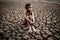 The boy sit hugging their knees bent and looking at the sky to ask for rain on dry soil