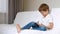 The boy sits on the bed, playing or watching a movie over the Internet using a tablet. The child experiences emotions of