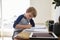 Boy Sits At Desk In Bedroom With Digital Tablet Doing Homework