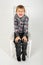 The boy sits and grimaces on a chair on a white background