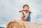 Boy sits on the haystack top with sunny sky background