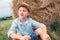 Boy sits near big haystack on the field