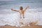 Boy sits on the ocean shore with his arms open towards wind and waves. Storm in summer, courage