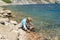 boy sits on shore of blue karst lake in the mountains
