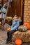 Boy sits on straw in the yard.He holds a pumpkin in his hands.Farmyard in autumn