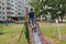 The boy sits at the top of a metal children`s slide and is going to slide down in the courtyard of a residential building