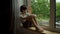 A boy sits at a wet window during the rain and looks at the street