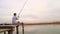 A boy sits on a wooden bridge and catches a fish on fishing rod.