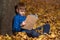 Boy sits in woods on fallen leaves and reading an exciting book. copy space mock up