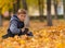 Boy sitting in brown fall leaves with skateboard.