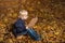 Boy sitting on fallen leaves in autumn forest with book. Child loves to read