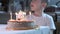 boy sitting at kitchen table and blowing candles on birthday cake, making wish