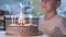 boy sitting at kitchen table and blowing candles on birthday cake, making wish