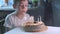 Boy sitting at kitchen table and blowing candles on birthday cake, making wish