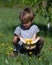 Boy sitting on knees holding hat with plucked dandelions on natural background. Looks at mosquito on finger.