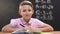 Boy sitting at school desk during math lesson and looking at camera, education