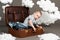 The boy is sitting in a suitcase and going on a journey, clouds of cotton wool as a decoration, gray background