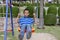 Boy sitting in the swings with a happy smile on the playground.