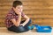 The boy is sitting by the toilet for kittens and thinks, against the background of a wooden wall