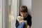 Boy sitting on the windowsill and hugs his favourite teddy bear