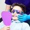 A boy in special glasses in the dentist`s chair. the doctor in sterile gloves shows him his smile in the mirror