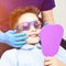 A boy in special glasses in the dentist`s chair. the doctor in sterile gloves shows him his smile in the mirror