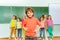 Boy stands in front of kids near blackboard