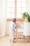 The boy stands next to the cot in the nursery and peeks. Lonely baby is in kindergarten near the crib. Loneliness. Eco-friendly ch