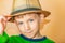 A boy in a straw hat and green clothes on a beige background takes off his hat in greeting