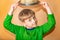 A boy in a straw hat and green clothes on a beige background takes off his hat in greeting