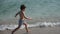 boy in striped swimming trunks runs along a sandy beach by the sea in summer