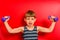 A boy in a striped t-shirt goes in for sports with purple dumbbells on a red background