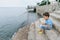 Boy in a striped T-shirt at the seaside breakwater block. boy standing on the beach. kid stands on a rock by the sea