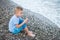 Boy in a striped t-shirt sitting close by the water at the beach