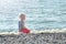 Boy in striped vest sits on a rock by the sea. Back view