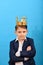 Boy in a suit and with a gold crown on his head on a blue background. domination and power over others