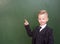 Boy in a suit points on empty green chalkboard