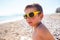 A boy in sunglasses plays on the beach