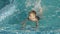 Boy swimming in the pool and kicking with their legs splashing the water