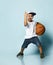 Boy in t-shirt, cap, shorts and sneakers. Holding basketball ball, smiling, showing three fingers, posing on blue background