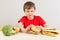 Boy at the table chooses between fastfood and healthy diet