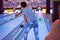 A boy throws balls at a bowling alley, knocking down pins