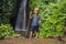 Boy with a trekking stick on the background of Leke Leke waterfall in Bali island Indonesia. Traveling with children