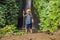 Boy with a trekking stick on the background of Leke Leke waterfall in Bali island Indonesia. Traveling with children