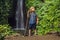 Boy with a trekking stick on the background of Leke Leke waterfall in Bali island Indonesia. Traveling with children