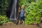 Boy with a trekking stick on the background of Leke Leke waterfall in Bali island Indonesia. Traveling with children concept