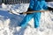 The boy is trying to shovel a snow disaster around the house. He holds in his hands a shovel, a spade and works in the snow in a b