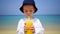 Boy of two years drinking mango fresh on the beach on the background of the ocean.