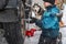 Boy unscrews nut on the wheel car. Replacing wheels in winter day on the background - house and siberian husky dog